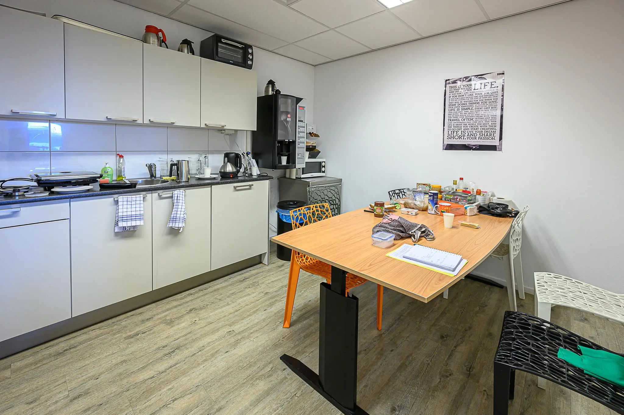 Kleine kantine of kantoorruimte met een kitchenette, koffieautomaat en tafel vol etenswaren en spullen.